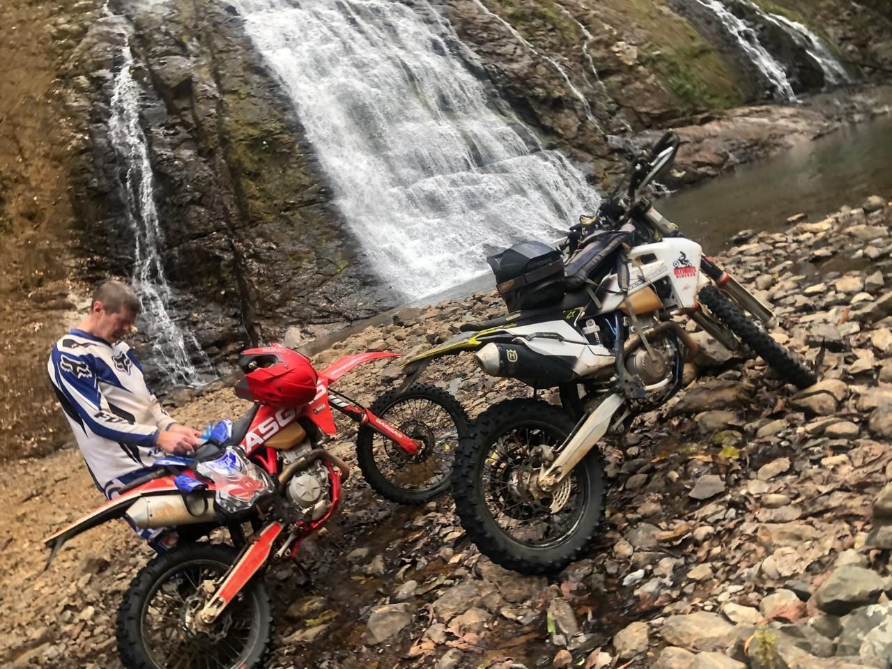 Two enduro motorcycles parked beside a jungle waterfall in Costa Rica during an Ultimate Rides CR tour