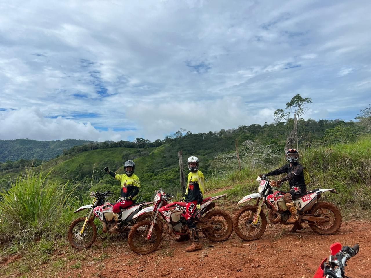 Three riders on enduro motorcycles on a mountain trail overlooking Costa Rica's rainforest hills