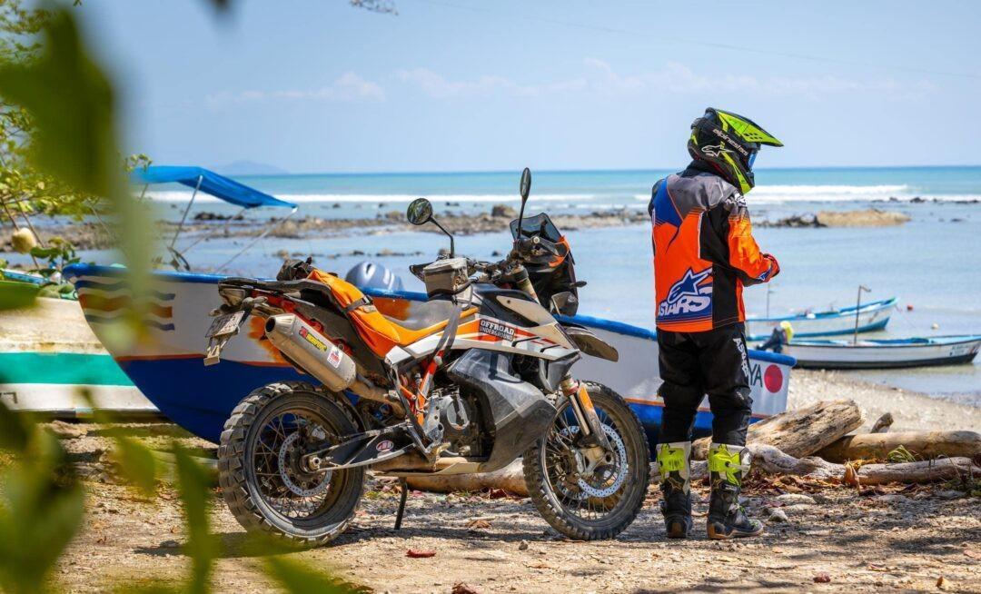 Adventure motorcycle parked beside a fishing boat on a Pacific coast beach in Costa Rica