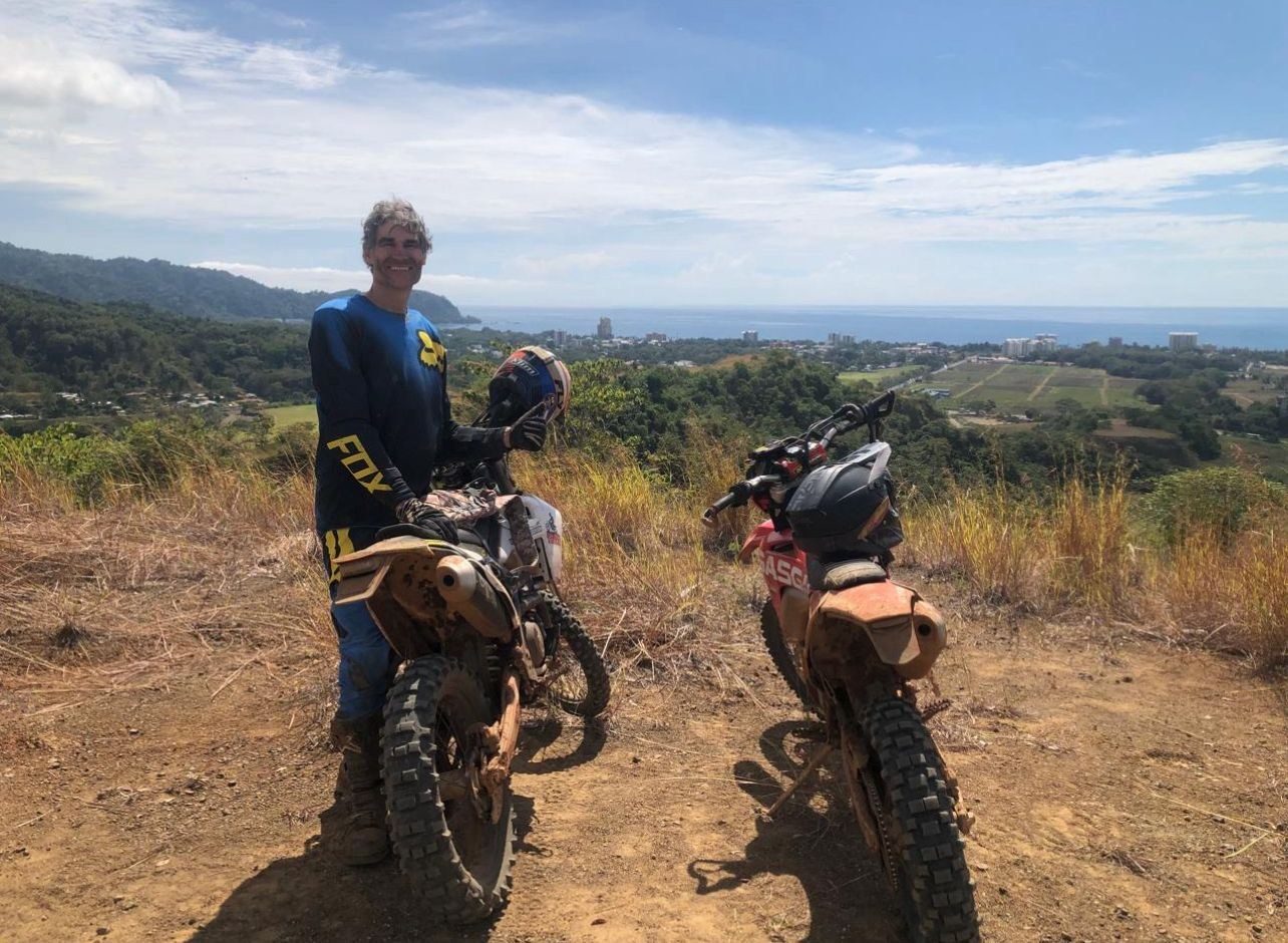 Rider with an enduro motorcycle overlooking Jacó and the Pacific coastline from a mountain trail